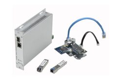 Elektronische Hardware-Komponenten, darunter eine graue Box mit Ethernet-Anschlüssen, zwei kleine Modulsteckplätze und eine Leiterplatte mit Kabelverbindungen.