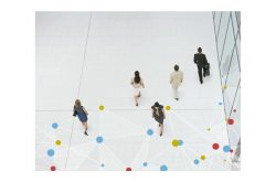 Fünf Personen gehen in einem modernen Gebäude mit weißen Fliesenböden, dekoriert mit bunten Kreisen und Linien.