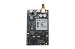 Ein elektronisches Modul mit der Aufschrift "Telit GE910-QUAD", mehreren Kondensatoren und einem goldfarbenen Anschluss oben.