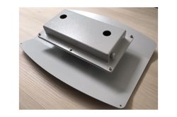 Ein grauer Metallkasten mit zwei Löchern auf einer rechteckigen Basis, auf einem Holztisch platziert.