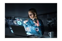 Eine Frau arbeitet an einem Laptop mit holografischen Diagrammen und Grafiken im Dunkeln.