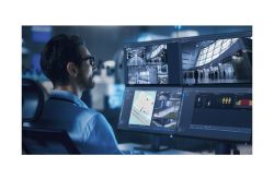 Ein Mann sitzt vor mehreren Bildschirmen mit Überwachungskameraaufnahmen und Sicherheitssoftware.