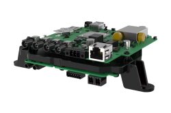 Eine grüne Leiterplatine mit mehreren Steckverbindern und elektronischen Bauteilen, darunter Ethernet- und Audiobuchsen, auf einer schwarzen Halterung montiert.