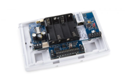 Elektronisches Gerät mit offenen Gehäuse auf einem weißen Kunststoffrahmen montiert, zeigt eine blaue Leiterplatte, Batteriefach und elektronische Komponenten.