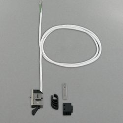 Verschiedene elektronische Komponenten, darunter ein Mikroschalter mit weißen Kabeln, eine schwarze Abdeckung und ein kleines rechteckiges Metallteil, auf einer grauen Oberfläche angeordnet.