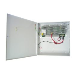 Geöffneter weißer Metallkoffer mit einem elektrischen Schaltnetzteil innen, verbunden mit roten und schwarzen Kabeln, sowie einer grünen Erdungskabelverbindung.